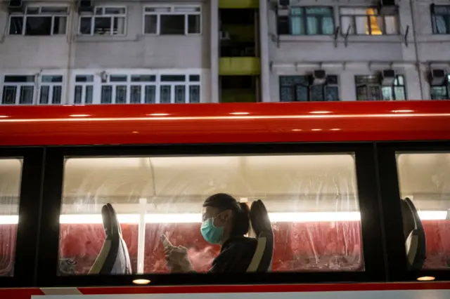 A passenger wearing a protective mask uses her phone on bus