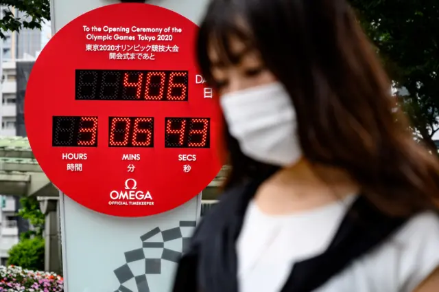 A woman wearing a face mask walks in front of a countdown clock of the Tokyo 2020 Olympics games in Tokyo, 12 June 2020