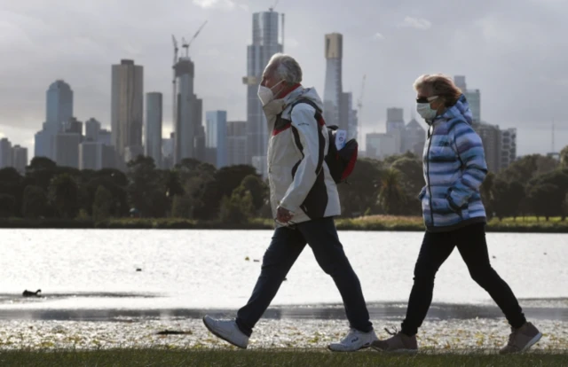 Melbourne residents wearing masks walk past a lake in the city