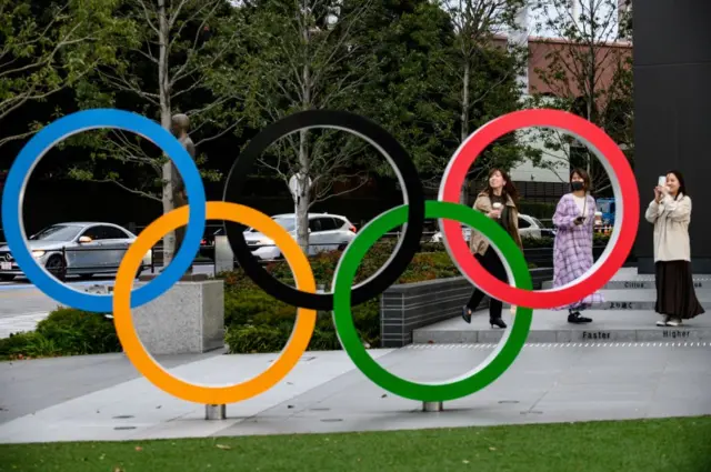 People take pictures of the Olympic Rings outside the closed Japan Olympic Museum in Tokyo on March 27, 2020,