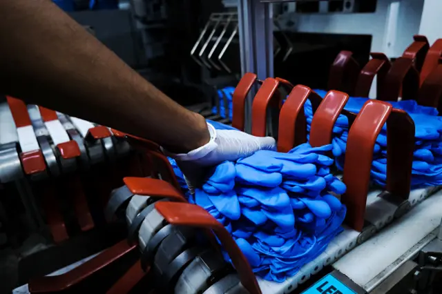 An employee moves bundles of latex gloves from an automated production line at a Top Glove Corp factory in Malaysia