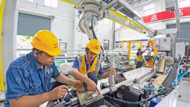 Men in yellow hard hats work on factory machinery in China.