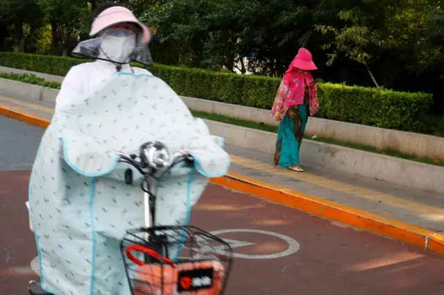 A woman wearing a mask rides on a scooter