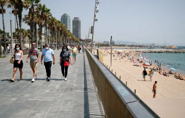 People wearing masks walk alongside a beach in Barcelona