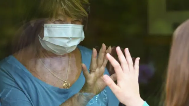 A woman with a mask on touching a family member through glass