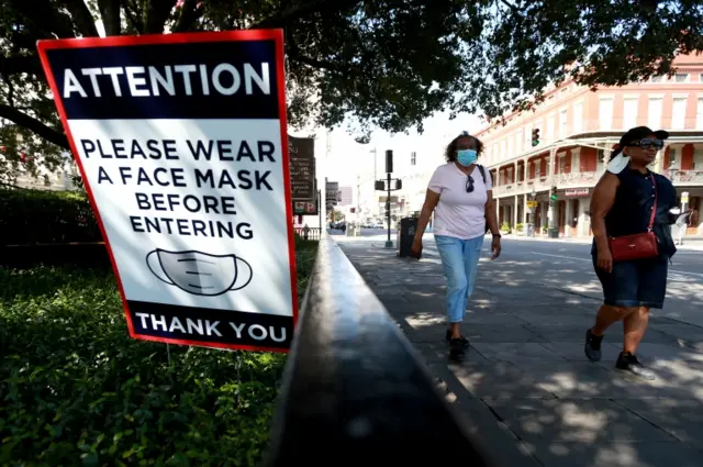 People in New Orleans, Louisiana, walk past a sign urging everyone to wear a face mask indoors