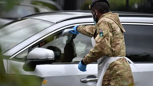 A member of military personnel passes self-test kits to members of the public through the window of a car at a COVID-19 drive-through mobile testing unit set up at Evington Leisure Centre in Leicester, central England on June 29, 2020