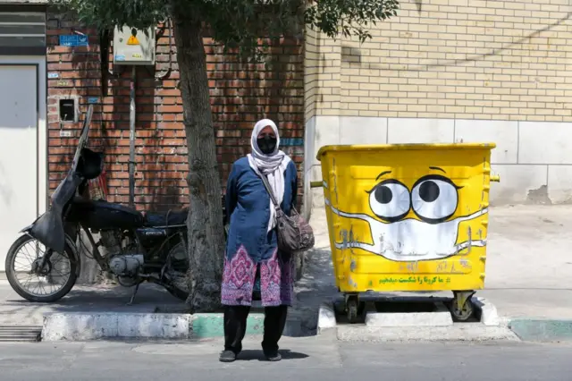 An Iranian woman stands next to a street bin in the capital Tehran