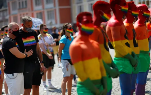 People stand wearing rainbow flags