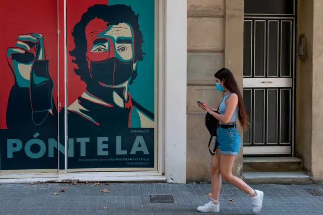 A woman walks past a sign reading "wear it" in Barcelona