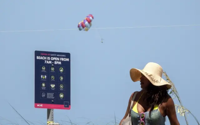 A woman walks past a sign for altered beach opening times