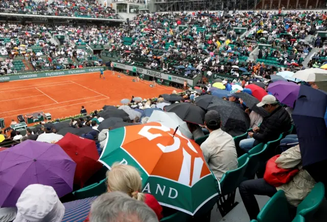 Fans shield from the rain with umbrellas during the quarter final match against Argentina"s Diego Schwartzman and Spain"s Rafael Nadal in 2018