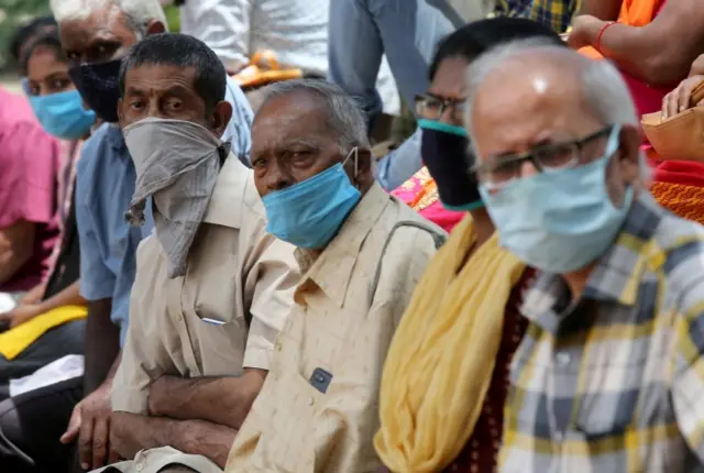 People wearing face coverings wait to collect free food and essentials in Bangalore in June