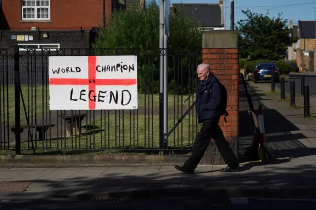 Man walks past England flag on fence