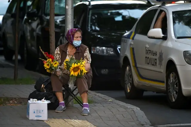 An elderly woman wearing a face mask to protect against the coronavirus disease sells flowers