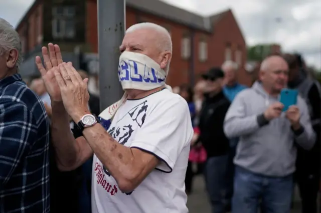 Man with England scarf over face applauds