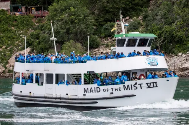 US passengers, wearing blue ponchos, are packed together on a ferry boat which is allowing 50% of its normal capacity