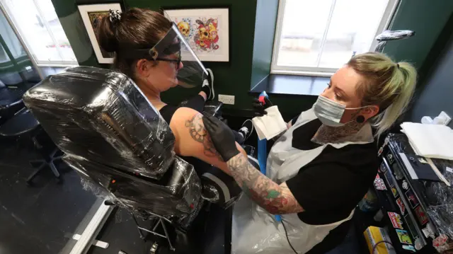 Tattoo artist Nikki Hilton from Heaven n Hell tattoo studios in Falkirk with client Ashley Mcara as Scotland continues with the gradual lifting of restrictions to ease out of lockdown.