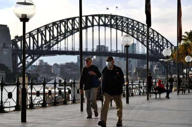 A man wears a mask in front of Sydney Harbour Bridge