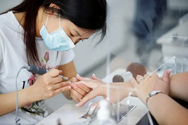 A nail technician wearing a protective mask works on a clients manicure