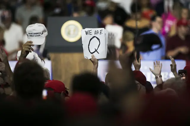 An attendee holds signs with the words "We Are Q" before the start of a rally with U.S. President Donald Trump