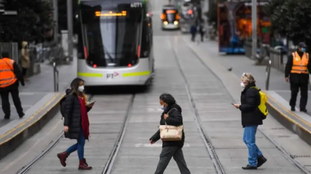 People wearing masks walk across a central city street in Melbourne