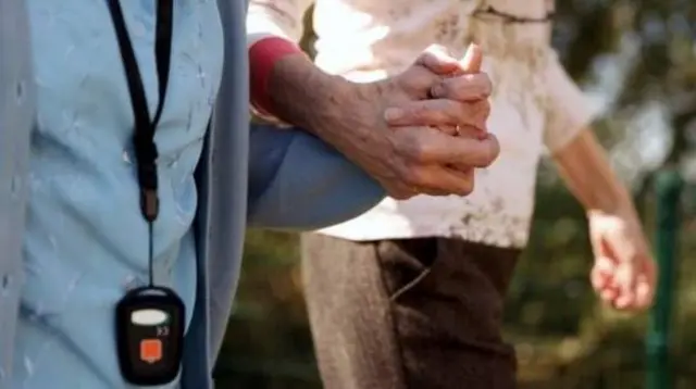 A helper holds the hand of an elderly person