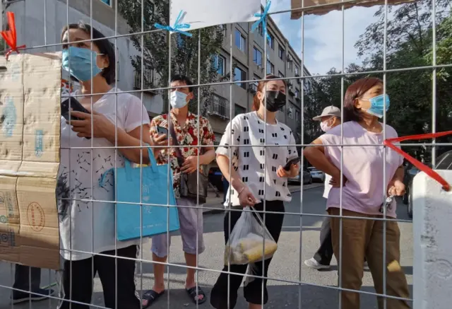 People wait for groceries to be delivered in a sealed compound