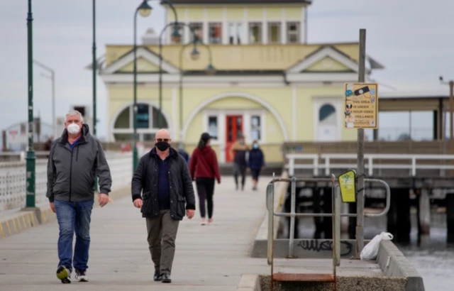 People wearing masks walk along a pier in Melbourne