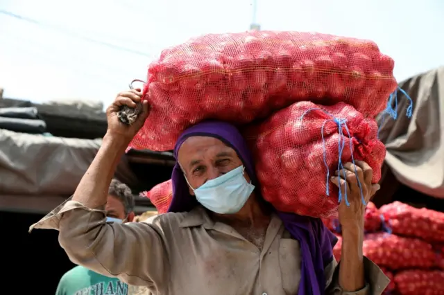 A man wearing a mask carries onions