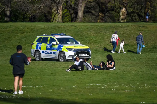 A police car in a park where people are sitting