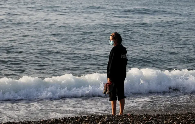 A woman wearing a face mask stands on a beach in Spain