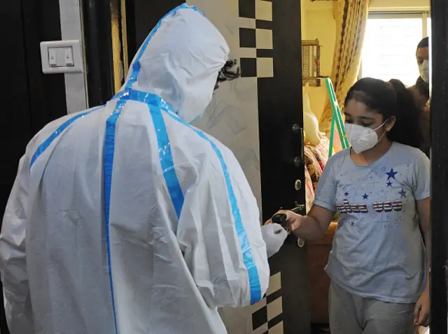 Healthcare worker wearing a personal protective equipment suit (PPE) checks oxygen level of a woman wearing a mask