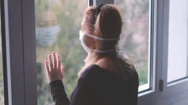 Woman wearing a mask looking through a window