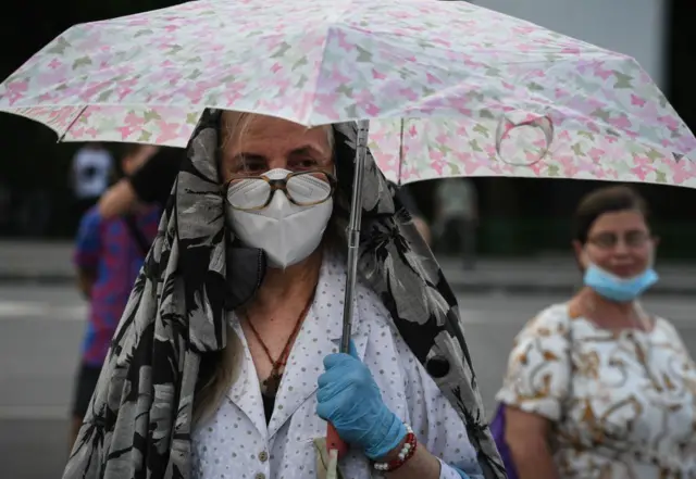 A woman in a face mask under an umbrella at a protest in Bucharest