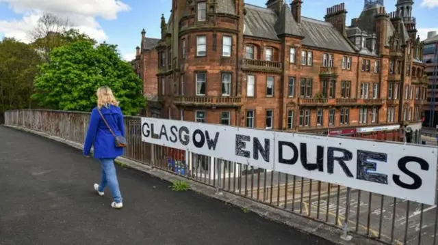 A woman walks past a 'Glasgow Endures' sign