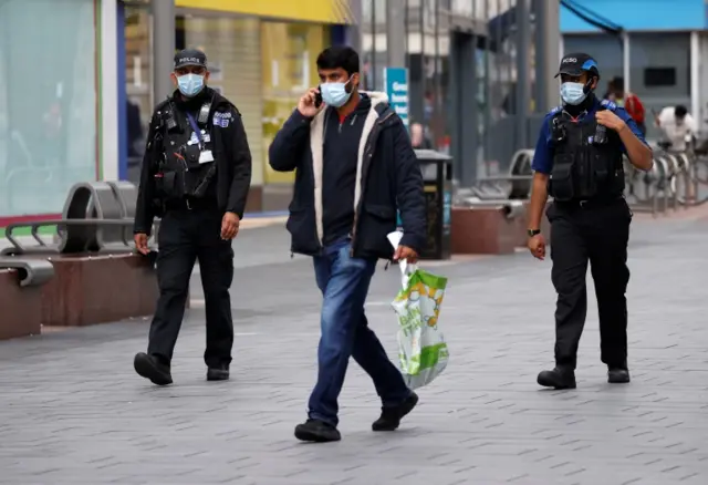 Police officers wearing protective masks patrol along a street in Leicester