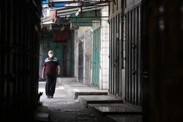 A Palestinian man walks near closed shops in an empty street, in the West Bank city of Nablus, 02 July 2020