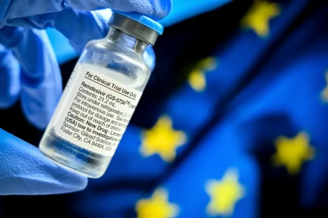 A vial of Remdesivir is shown in front of an EU flag