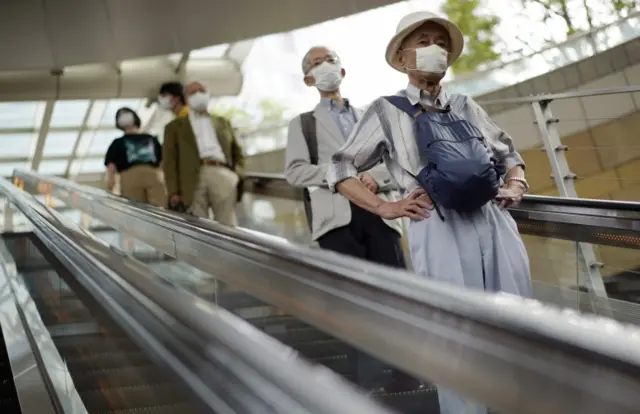 People wearing masks ride an escalator at Roppongi district in Tokyo, Japan