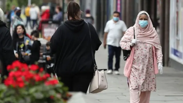 A woman walking down the street with a face mask and gloves