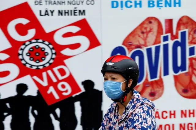 A woman walks past a banner promoting prevention of Covid in Hanoi