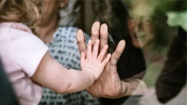 A baby and elderly person pressing their hands against a window