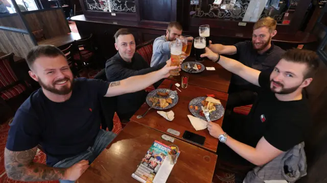 A group of customers give a toast with their drinks at the Shakespeare"s Head pub in Holborn, London, as it reopens for business as coronavirus lockdown restrictions are eased across England