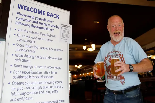 A customer reacts as he walks with two pints of beer past an information board giving advice on new anti-covid measures inside the Wetherspoon pub, Goldengrove in Stratford in east London