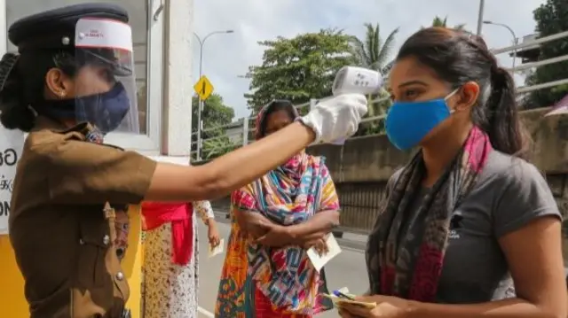 A Sri Lankan police officer checks the body temperature of a woman in Colombo. Photo: June 2020