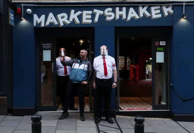 A man gives thumbs up as he stands outside a pub with bouncers