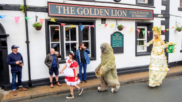 Street artists perform for costumers outside the Golden Lion pub in Todmorden, West Yorkshire, as it reopens following the easing of coronavirus lockdown restrictions across England.