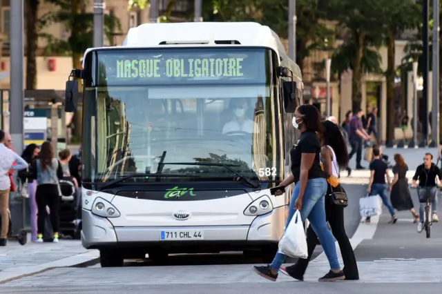 Women wearing a protective face mask walk past a bus with the display reading 'Mask is compulsory' in Nantes