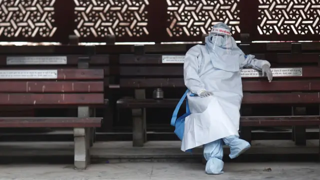 A person in full PPE in New Delhi rests before the cremation of a man who died of Covid-19